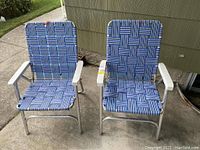 Front view of two vintage folding lawn chairs with blue woven fabric seats and backs, silver metal frames, and white armrests placed outdoors.