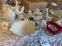 Wide shot of porcelain collection on lace tablecloth showing swan figurines, decorative vases, candy dish, Christmas ornaments and other figurines