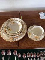 Top view of stacked Limoges china plates and teacup with saucer showing yellow daisy pattern and gold trim. Partial stainless steel flatware pieces displayed in front.