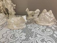 Pearlized ceramic animals including cow, donkey, and a mountain representation on a lace-covered surface.