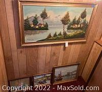 Large framed oil painting of ocean landscape with houses and trees hung on wood panel wall, shows overall lot context
