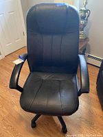 Front view of black leather-like office chair with padded armrests and rotating wheel base on wooden floor.