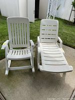 Front view of white plastic outdoor rocking chair and patio lounger side by side on pavement outdoors.
