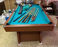 Front angle view of pool table showing cues, balls, and accessories on table surface