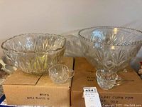 Two punch bowls, two punch cups in front, boxes underneath, plastic ladle visible inside one bowl.