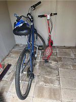 Shows blue Schwinn bicycle with black seat, bike lock coiled around handlebars, blue and black helmet resting on saddle, and red Razor E100 electric scooter next to bicycle.