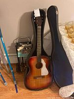 Silvertone acoustic guitar standing in open guitar case with travel caddy visible in background