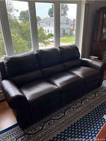 Full view of the three-seat dark brown leather-like sofa near window, showing overall size and style.