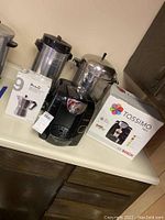 Tassimo coffee maker with box, espresso coffee maker, and two metal coffee urns on counter