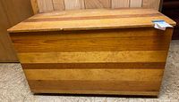 Front view of a rectangular wooden storage trunk with horizontal wood paneling in natural wood tones.