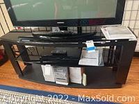 Front view of black 3-tier TV stand holding a flat-screen TV and various items on shelves.