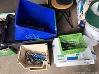 Various black handle screwdrivers and pliers in green and beige bins among scattered tools