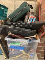 View of different automotive tools and parts organized in storage bin, including lug wrench, belts, packaged items, and a green zippered bag