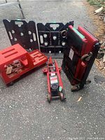Full lot view showing the hydraulic trolley jack, red toolbox, two black plastic racks, and the Team Mechanix creeper in standing position.