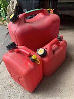 Three red plastic Jerry gas cans of varying sizes arranged on the ground