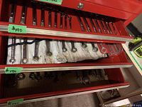 Three open red metal drawers with hand tools including combination wrenches and sockets, some labels visible.