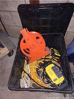 Overall view of black storage box containing orange cord reel, NOMA power bar, and various extension cords in yellow and white.