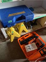 Overall view showing blue cleaning kit case, yellow jack stands, and orange nailer case on shelf.