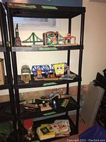 Front view of resin shelving unit loaded with various toy items, showing height, shelf spacing, and black resin construction.