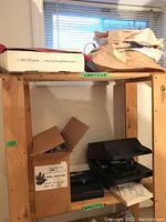 Wood shelving unit with various items including a large box, a black case, and brown wrapping paper on top. Shelving contains additional boxes and possibly tools or parts stored inside.