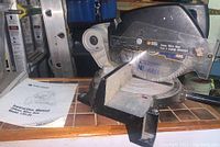 Wide shot showing the mitre saw on a wooden surface with instruction manual beside it.