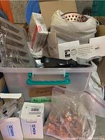 Plastic bin with various plumbing parts and accessories including copper clips and boxed Moen parts.