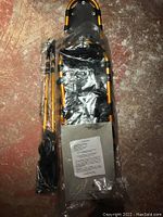 Photo of packaged magnesium snowshoes and poles on a floor showing the full length of one snowshoe and poles inside clear plastic wrapping.