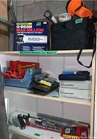 View of Q-Beam Max Million spotlight box, two vinyl-coated hook boxes, hand clamps, orange tool bag and red handled tools in blue bin on shelving.