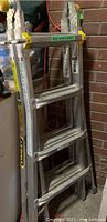 Full view of folded aluminum ladder with visible rungs and yellow locking parts, leaning against a wall in a garage.