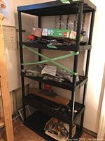 Front view of tall black resin shelving unit filled with assorted items and green tape across two middle shelves.