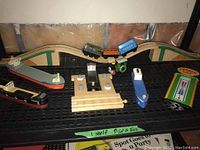 Overview of lot with wooden toy boats, railroad tracks, and thermometer arranged on black shelving grid.