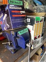 Blue Mastercraft vise model 5790052 mounted on a workbench next to boxed items including an anvil box.