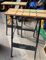 Overall view of two Ultra Steel foldable workbenches showing wooden tops with holes and yellow handles on sides.