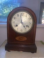 Front view of the antique mantel clock front showing wood case, inlaid decoration, clock face with Arabic numerals under glass cover