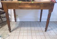 Full side view of antique pine wood table showing the center drawer and turned legs.