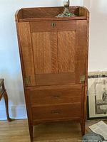 Front view of antique solid wood secretary desk showing closed drop front and two lower drawers with brass hardware.