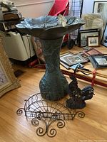 Full view of bird bath, rooster statue, and metal basket on wooden floor indoors with framed pictures in background