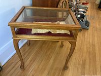 Full view of the wood display table with clear glass top, showing its natural finish and curved legs.