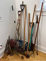 Wide shot of the garden tools in a corner including shovels, rakes, pruners, and an axe.