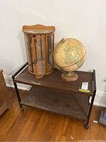 Photo of the three items: a vintage globe on a rusted metal base, a wooden wall display cabinet with curved glass door and glass shelves, and an MDF and metal rolling shelf with wheels.