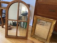 Photo of two wood framed mirrors; one arched divided into four sections, one smaller with gold decorative frame.