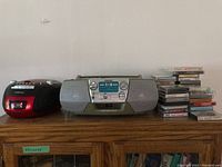 Wide view showing Sony CFD-V7 boombox, Audiovox CD cassette player, and cassette tapes stacked on wooden shelf.