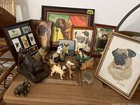 View showing collection of 7 framed dog prints and 11 dog figurines on a wooden surface, framed pieces vary in size and style, figurines include porcelain, metal, glass, and ceramic materials.