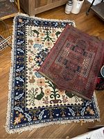 Two handmade wool rugs displayed together on wooden flooring, showing overall pattern and size comparison.
