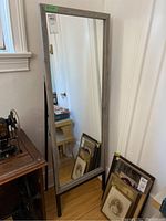 Full view of the standing mirror showing the wood frame and black metal easel support on a hardwood floor.