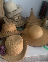 Six straw hats arranged on a table in various shapes and textures, showing style variety and condition.