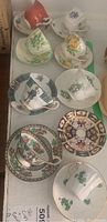 Photo showing all eight tea cup and saucer sets, arranged on a table. Various floral and shamrock patterns are visible.