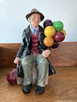 Front view of Royal Doulton The Balloon Man figurine, showing seated man holding balloons and red bag on left side