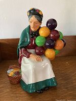Front view of the Royal Doulton balloon seller figurine showing the elderly woman holding colorful balloons, seated with a basket of fruit at her side.