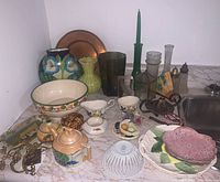 Photo showing 6 vases, various pottery items, brass drawer pulls, and other decorative items arranged on countertop next to sink.